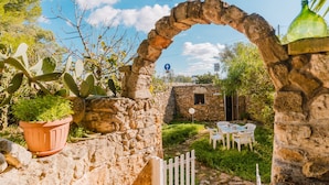 A stone archway leading to a patio with a table and chairs, surrounded by greenery and a potted plant. - Rustic Dwelling by Vivimy (Ugento)