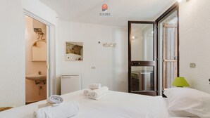 A hotel room with a bed, a bathroom, a green lamp, and a painting on the wall. - Rustic Dwelling by Vivimy (Ugento)