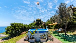A pool surrounded by potted plants, a wooden deck, and a view of the sea.