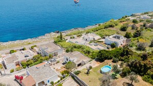 An aerial view of a coastal residential area with houses, a swimming pool, and a clear view of the sea.