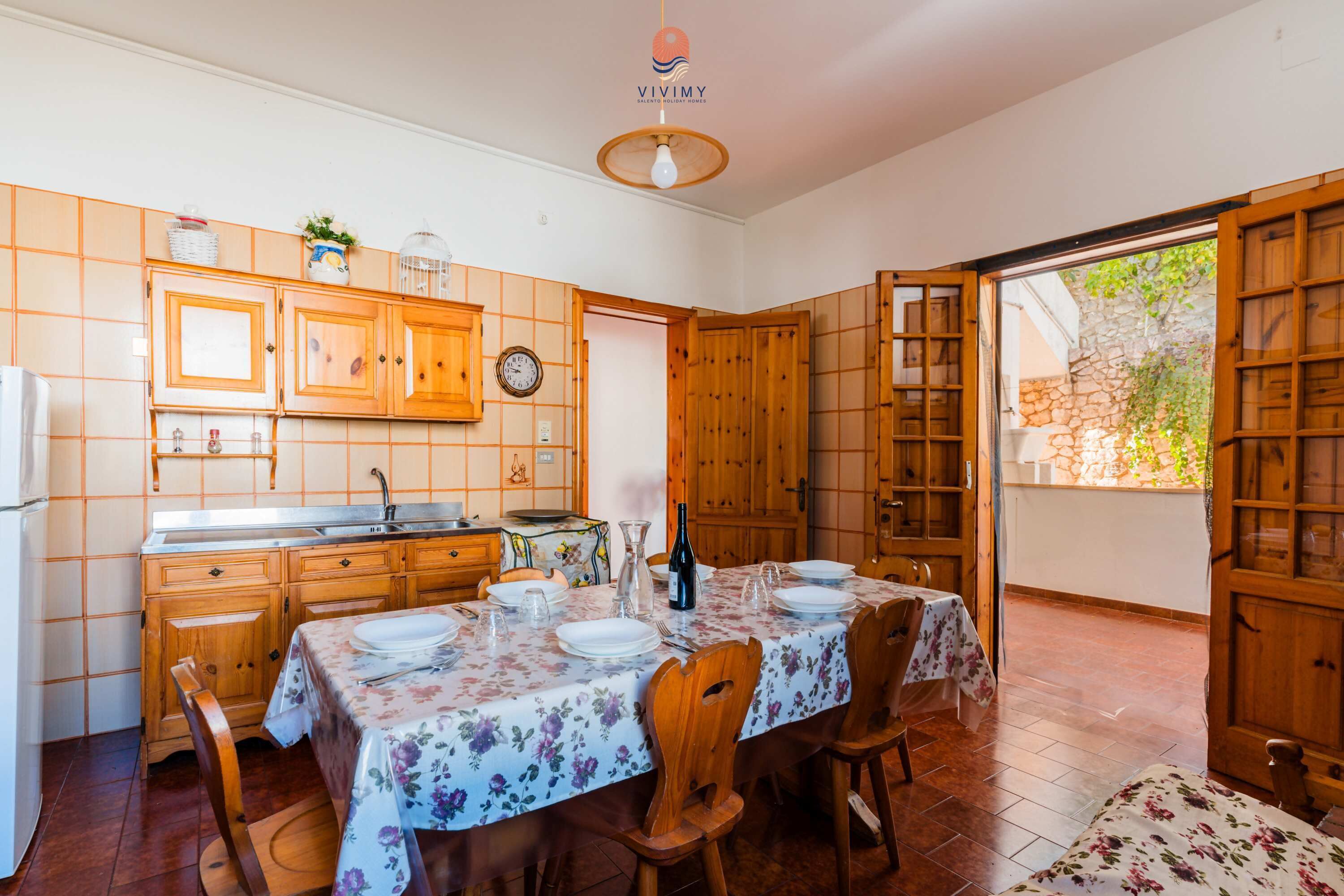Una cocina con armarios de madera, una mesa de comedor para cuatro personas y vistas al jardín a través de una puerta abierta.