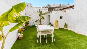 A small, enclosed garden with a white table and chairs, surrounded by potted plants and a white wall. - Nita House by Vivimy (Racale)