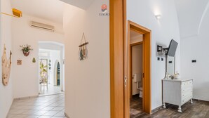 A hallway with a tiled floor, a wooden door, a white dresser with a flat-screen TV, and a wall-mounted air conditioner. - Nita House by Vivimy (Racale)