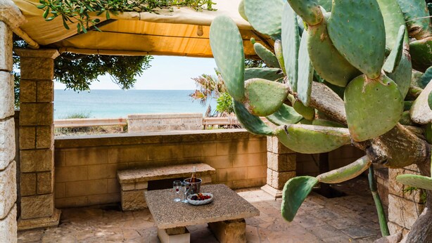Un patio in pietra con tavolo e panchina, vista sul mare.
