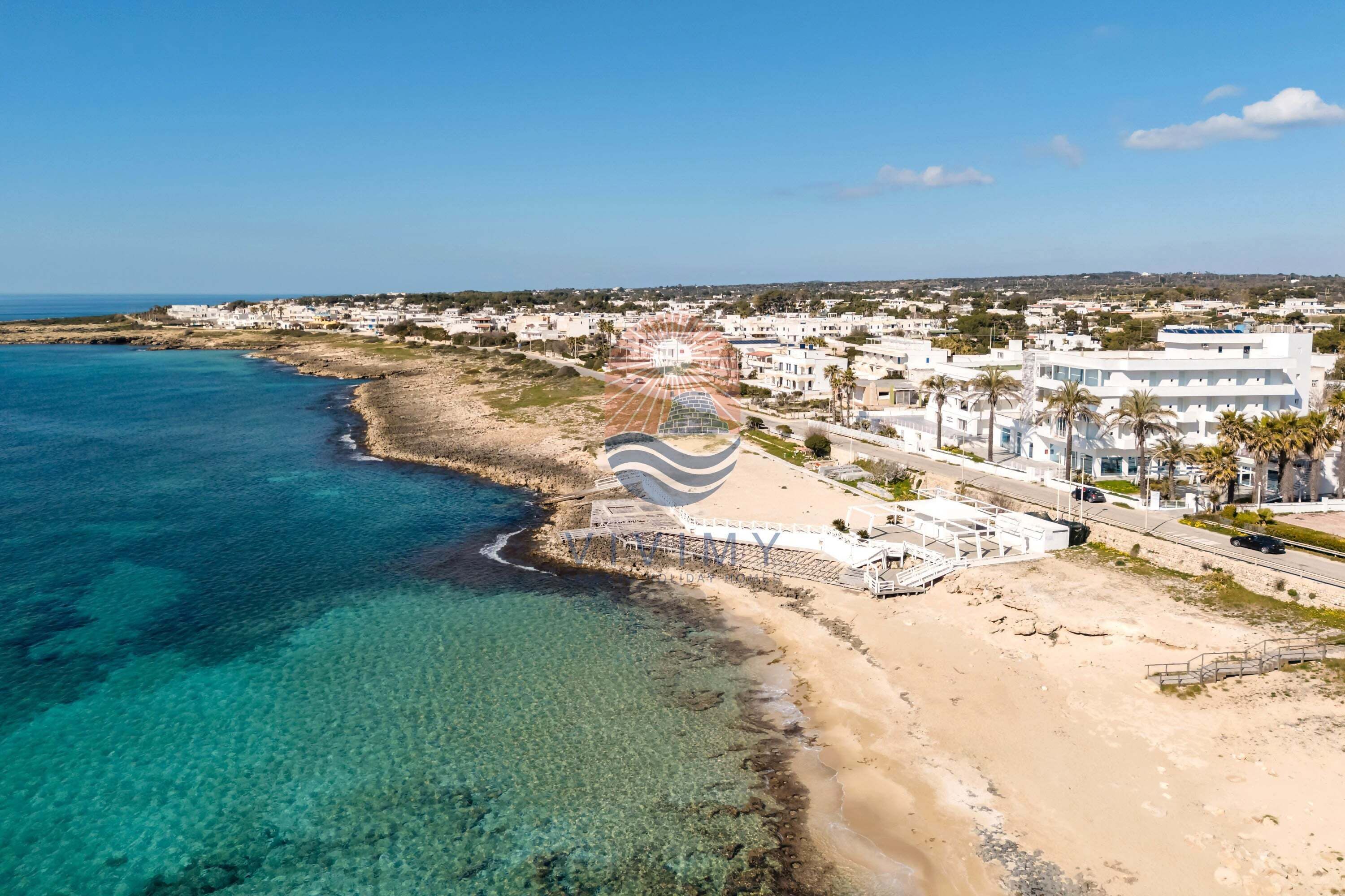 A coastal town with a beach, clear blue waters, and white buildings.