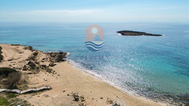Paisatge costaner amb una platja sorrenca, un promontori rocos i una mar blava i nítida.