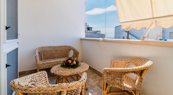 Ein Balkon mit Korbmöbeln, darunter eine Couch und zwei Stühle, sowie ein kleiner Tisch mit einem floralen Arrangement.