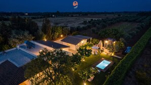 Ein Wohnhaus mit Swimmingpool, Solaranlage und einem gut beleuchteten Garten im Abendlicht.