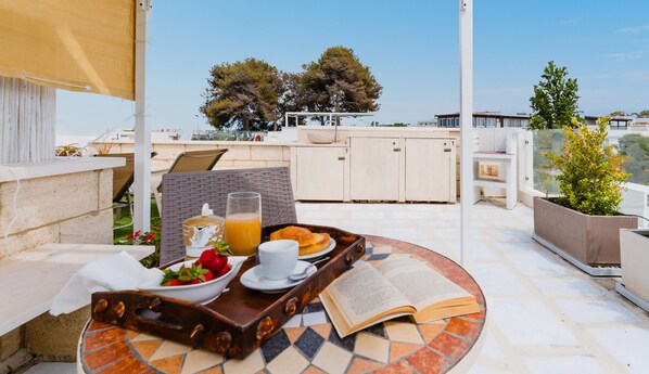 A terrace with a table set for breakfast, including a tray with strawberries, juice, and a book. - Elodie - Lido Marini by Vivimy (Lido Marini)