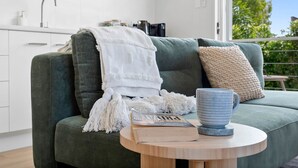 A modern living room with a green sofa, a white throw blanket, a blue mug, and a book on a wooden side table.
