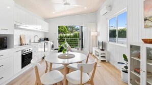 A modern kitchen with white cabinets, a dining area with a round table and chairs, and a large window with a view of greenery.