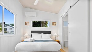 A bedroom with a bed, two bedside lamps, a window, an air conditioning unit, and a wardrobe.