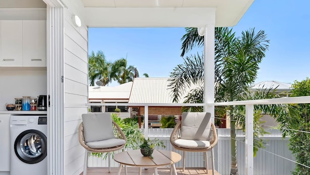 A patio with two wicker chairs, a small table, and a washing machine in the background.