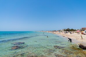 Una playa con agua cristalina, gente nadando y sombrillas en la arena.