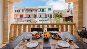 Ein Balkon mit einem Tisch, gedeckt für ein Frühstück, inklusive Croissants, Obst und Kaffeetassen.