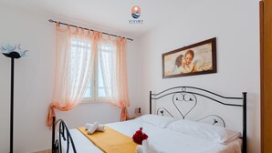 Ein ordentlich bezogenes Bett mit weißen Leinen und einer gelben Decke, ein gerahmtes Bild an der Wand und eine Stehlampe.