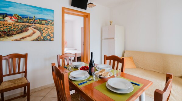 Un comedor con una mesa dispuesta para dos personas, un cuadro en la pared y un sofá al fondo.