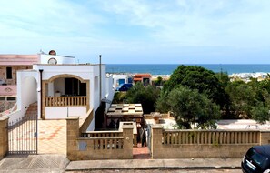 Un edificio costiero con una scala che conduce a un balcone, un cancello e vista sul mare.
