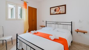 Une chambre à coucher comprenant un lit, une chaise, une armoire en bois, une fenêtre avec des rideaux, un tableau accroché au mur et des tables de chevet.