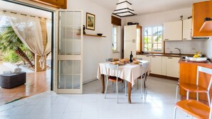 Een moderne keuken met witte kasten, een eettafel voor vier personen en een groot raam dat voor natuurlijk licht zorgt.