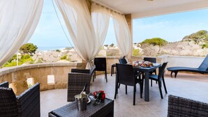 Een terras met rieten meubels, een gedekte tafel en uitzicht op zee.