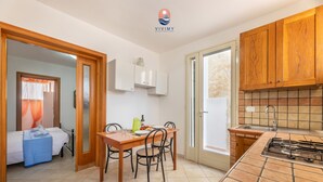 A compact kitchen with wooden cabinets, a tiled backsplash, and a small dining area with a table and chairs. - Siren - Mediterranean Verandas (Torre Vado)