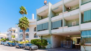 A multi-story hotel with a clear blue sky, parked cars, and palm trees. - Coral by Vivimy real estate (Gallipoli)