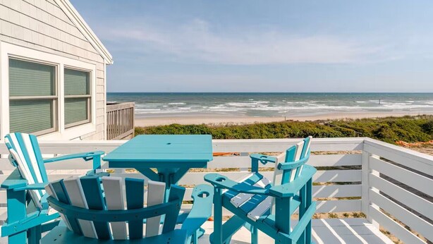 Eine Terrasse mit Tisch und Stühlen mit Blick auf einen Strand.