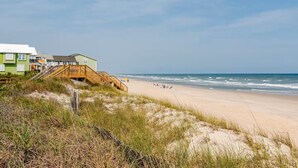 Ein Strand mit einer Holzpromenade, die zu einem Gebäude mit vielen Fenstern und einem grünen Dach führt.
