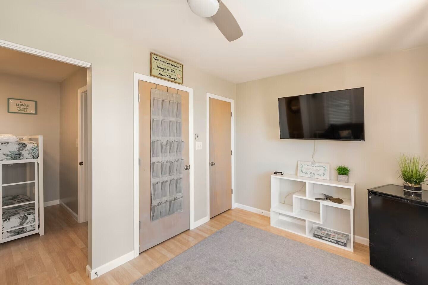 A modern living room with a flat-screen TV, a ceiling fan, and a grey rug.