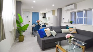 A modern living room with a grey sofa, a glass coffee table, and a dining area with a blue chair and a white table. - 1 minute to Universal Studios Japan! Spend a relaxing time in a stylish house with free parking! (Osaka city Konohana-ku Shimaya)