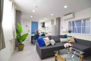 Ein modernes Wohnzimmer mit einem grauen Sofa, einem Glastisch und einem Essbereich mit blauem Stuhl und weißem Tisch.