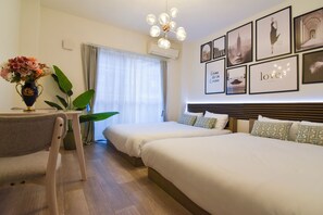 Ein Hotelzimmer mit zwei Betten, einem Esstisch, einer Vase mit Blumen und einer Wand mit gerahmten Bildern.