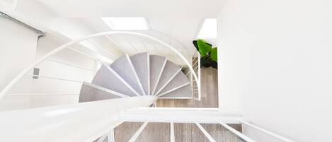 Una escalera de caracol con barandilla blanca que asciende en un interior moderno.