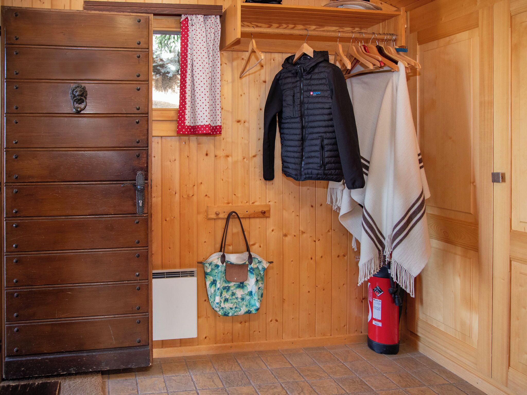 A wooden room with a wardrobe, a hanging coat rack, a fire extinguisher, and a bag.