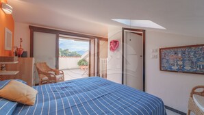 A bedroom with a bed, a chair, a small table, a door leading to a balcony, and a wall with a decorative item. - Il Porto 19 - Mansarda sul Mare (Porto Azzurro)
