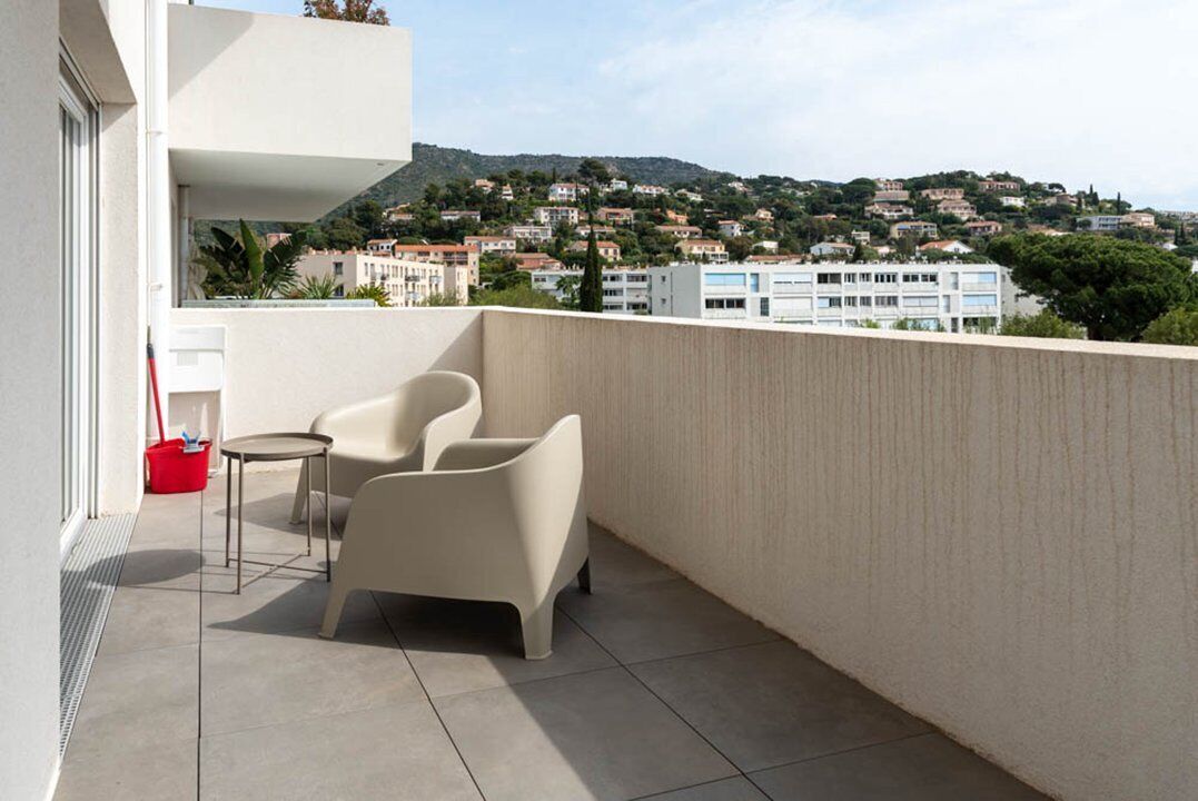 A balcony with two chairs and a small table, overlooking a hillside with buildings.