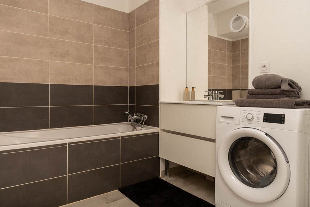 A modern bathroom with a bathtub, a washing machine, and a mirror.