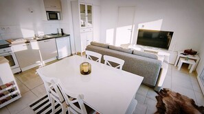 A modern kitchen with white cabinetry, a dining table with chairs, a sofa, a TV, and a dog lying on the floor. - Rental of a T3 for 6 in a residence with swimming pool, 900m from the beach. (LE LAVANDOU)