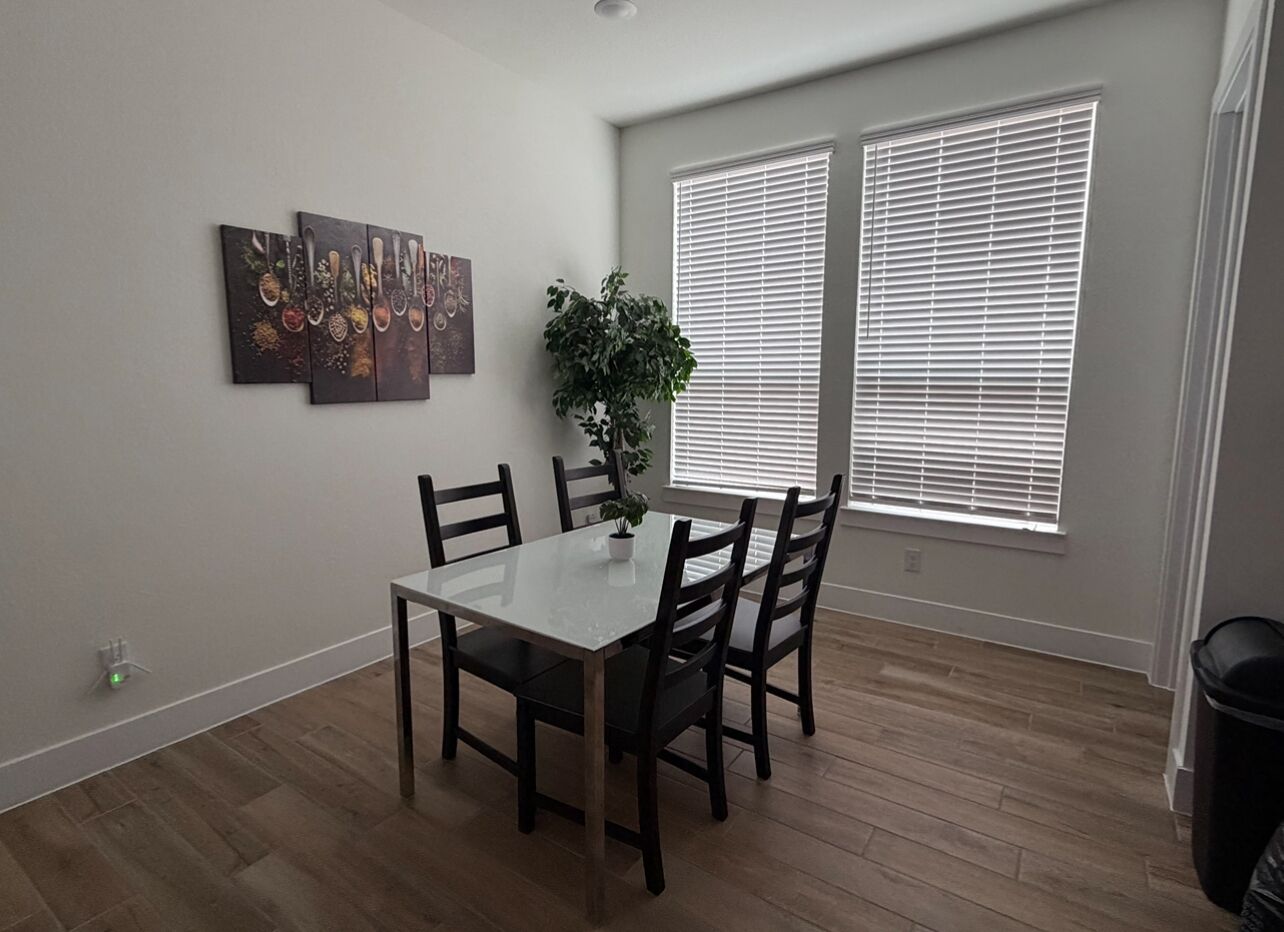 Un coin repas comprenant une table rectangulaire, quatre chaises, une plante en pot et des œuvres d’art accrochées au mur.