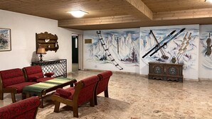 Eine Lobby mit Holzvertäfelung, einer Gebirgsmalerei, einer Holzbank und einem kleinen Tisch mit einer Lampe.