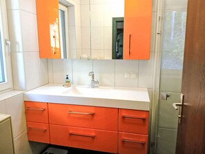 Une salle de bain avec un lavabo blanc, des meubles orange et un grand miroir.
