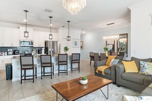 A modern kitchen with white cabinets, a central island, and pendant lighting. There is a dining area with a gray sofa and a coffee table. - Family Private Pool Villa Near Disney & Universal
BBQ+Resort+LazyRiver+Waterpark (Kissimmee)