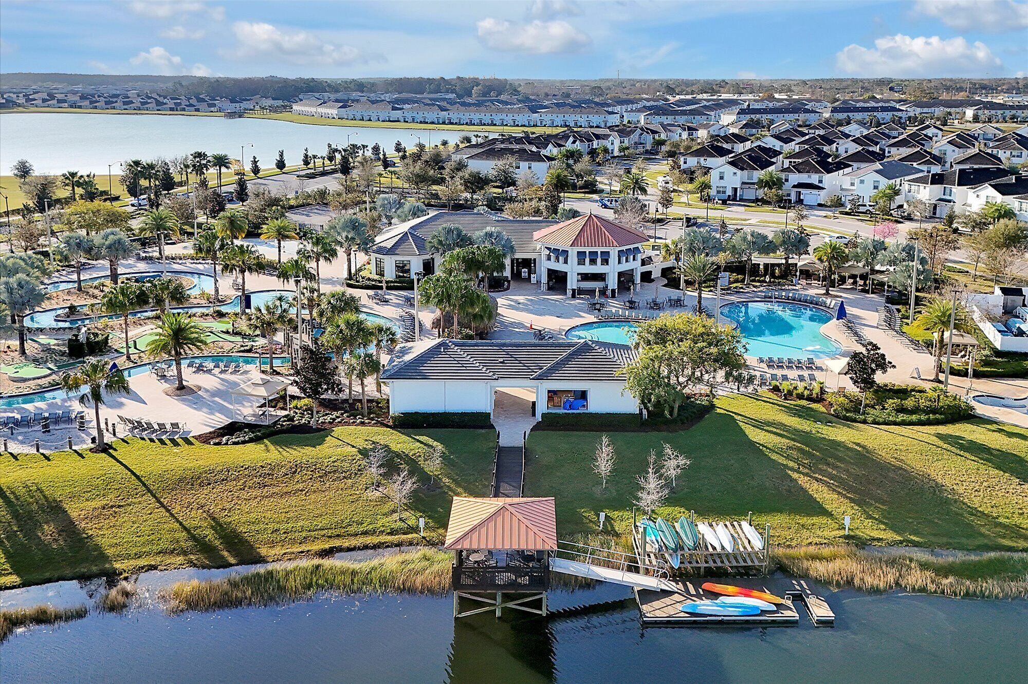 Un resort con varias piscinas, un muelle con kayaks y un edificio grande con un techo característico.