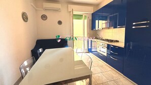 Una cocina moderna con armarios azules, encimera blanca y un comedor con mesa y sillas de vidrio.