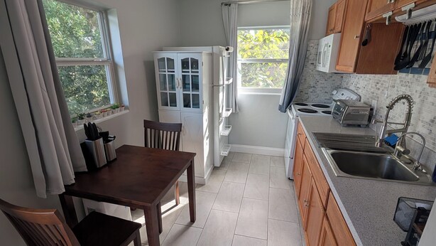 A compact kitchen with a dining area, featuring a window, cabinets, and a microwave. - The Guesthouse on Mills 50 (Orlando)