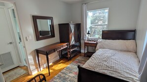 A bedroom with a bed, a desk, a chair, a wardrobe, a ceiling fan, and a window. - The Guesthouse on Mills 50 (Orlando)