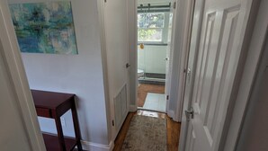 A hallway with wooden flooring, white walls, and a door leading to a bathroom. - The Guesthouse on Mills 50 (Orlando)