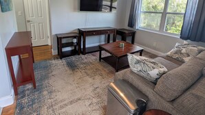 A living room with a sofa, coffee table, TV, ceiling fan, and a window with curtains. - The Guesthouse on Mills 50 (Orlando)