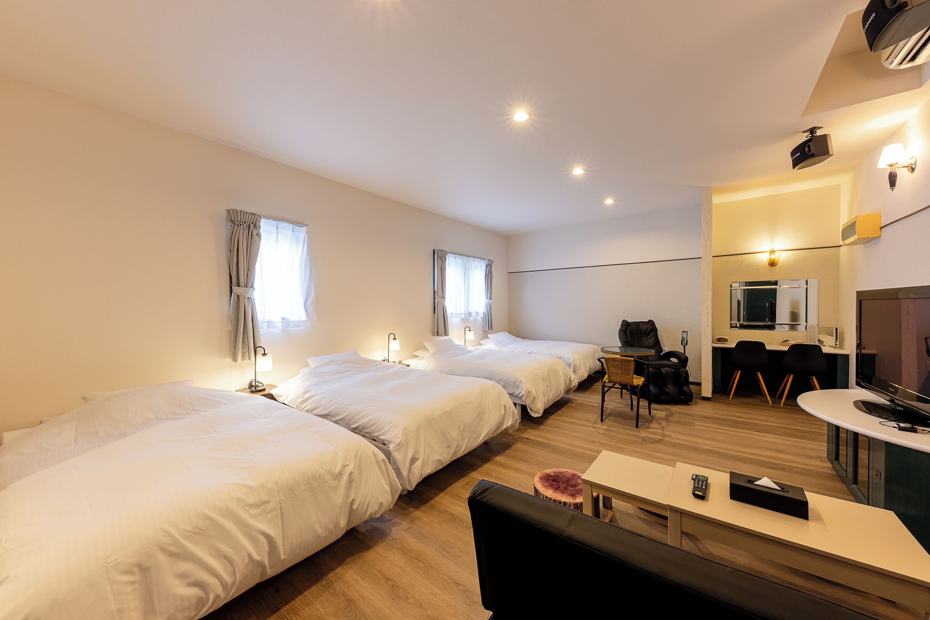 Une chambre d’hôtel avec trois lits, un bureau, une chaise, une télévision et une kitchenette.